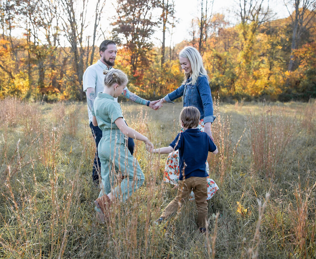 A family holds hands and dance in a circle during their lifestyle family session in the Jerusalem Mill field in Kingsville, Maryland