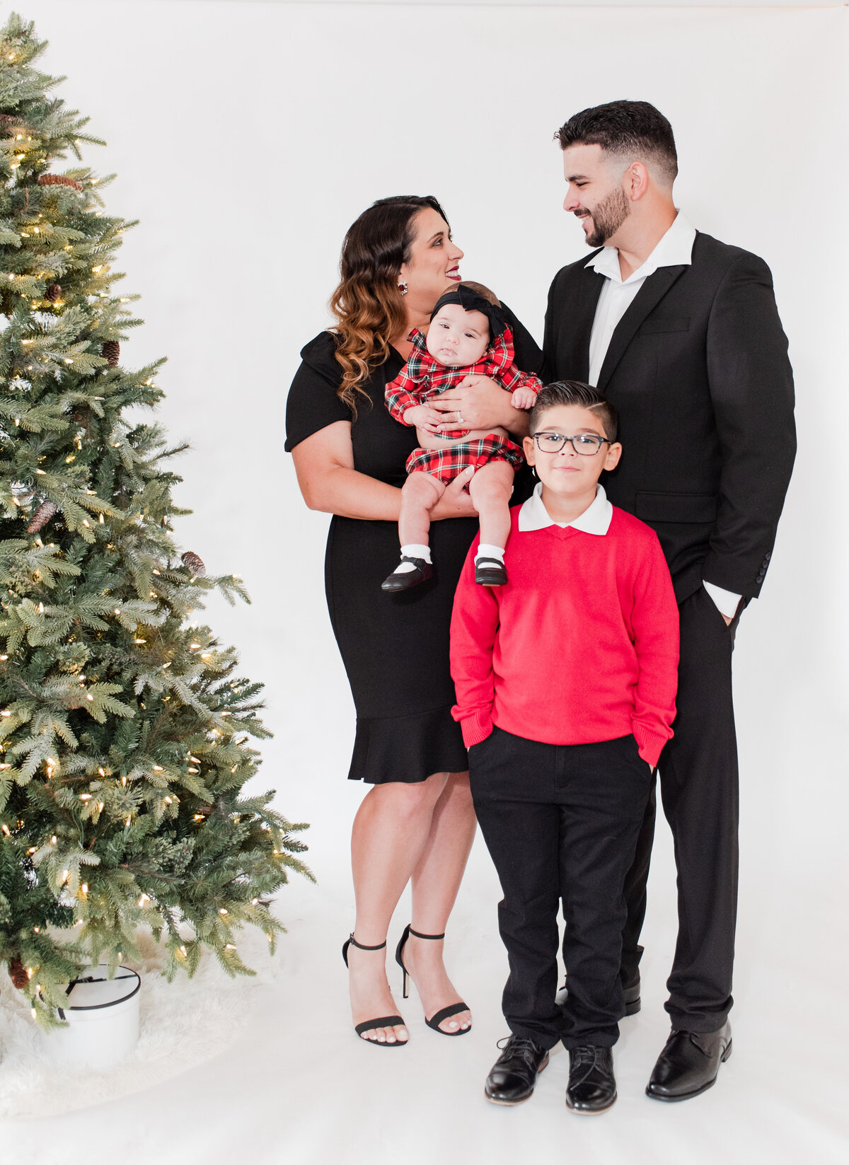 family of four in front of a Christmas Tree by Miami Christmas Mini Session Photographers