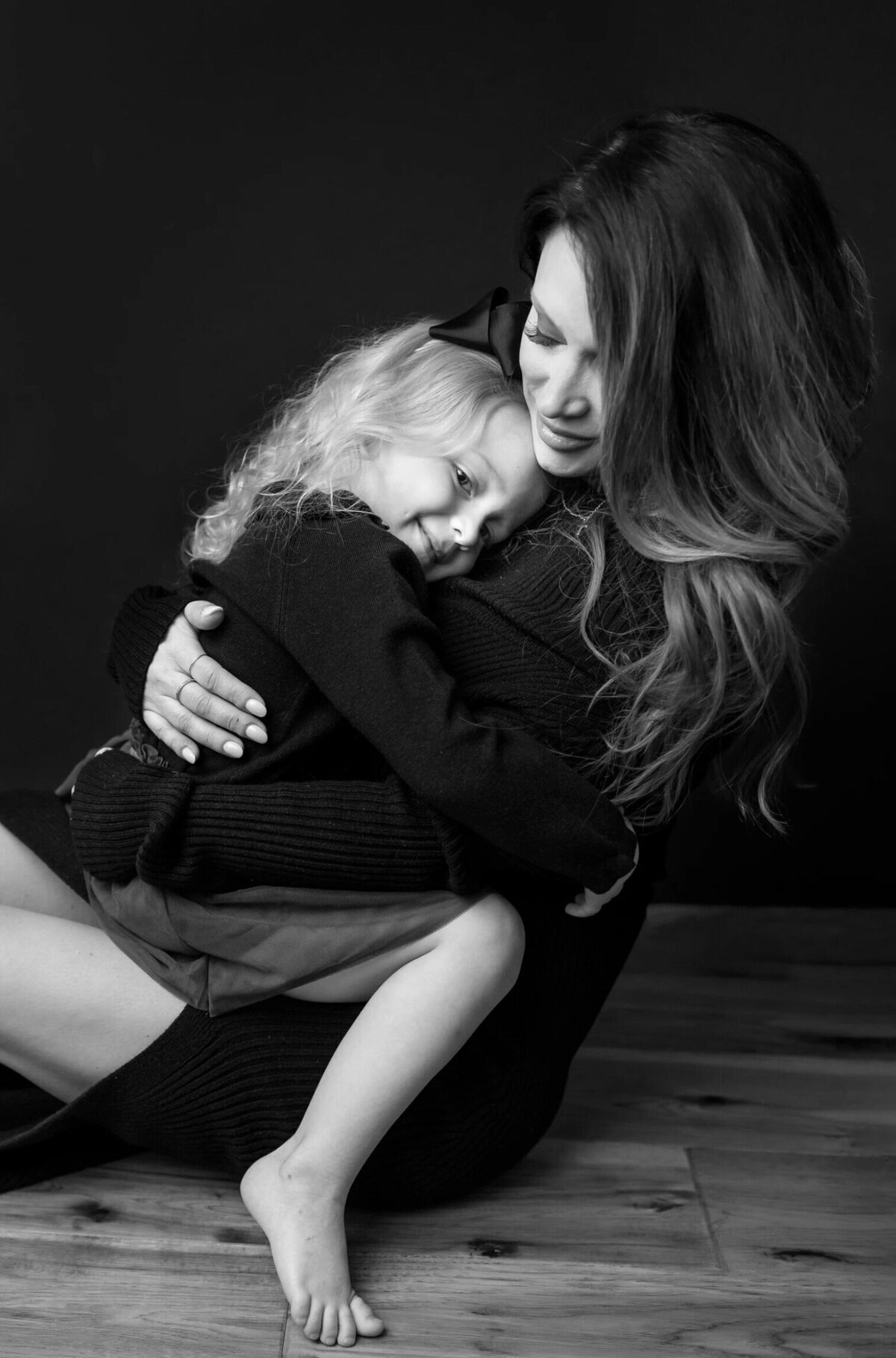 Mother holding her young daughter, both wearing black on a black background