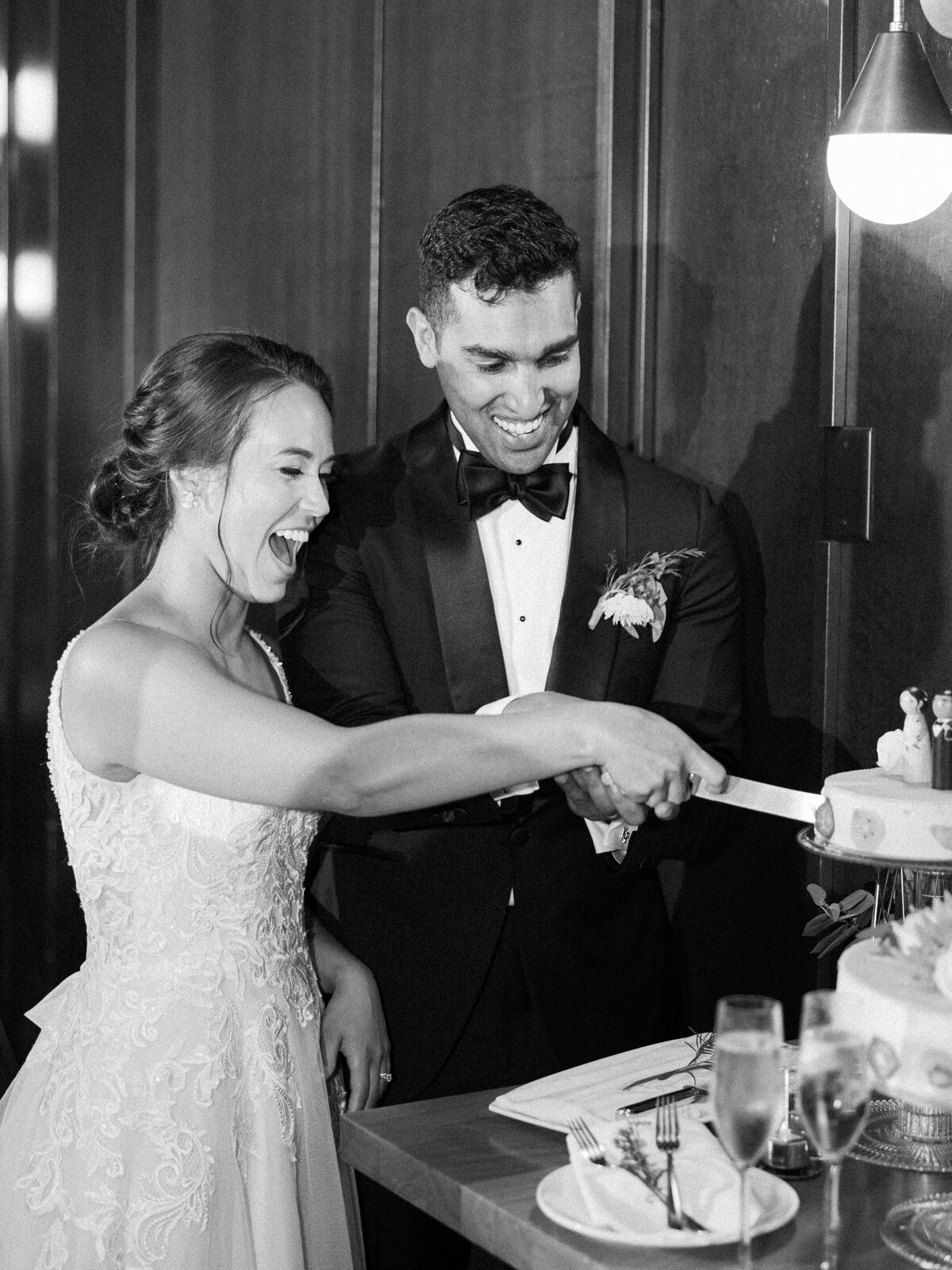 A bride and groom smile ear to ear as they cut their wedding cake together during their wedding reception