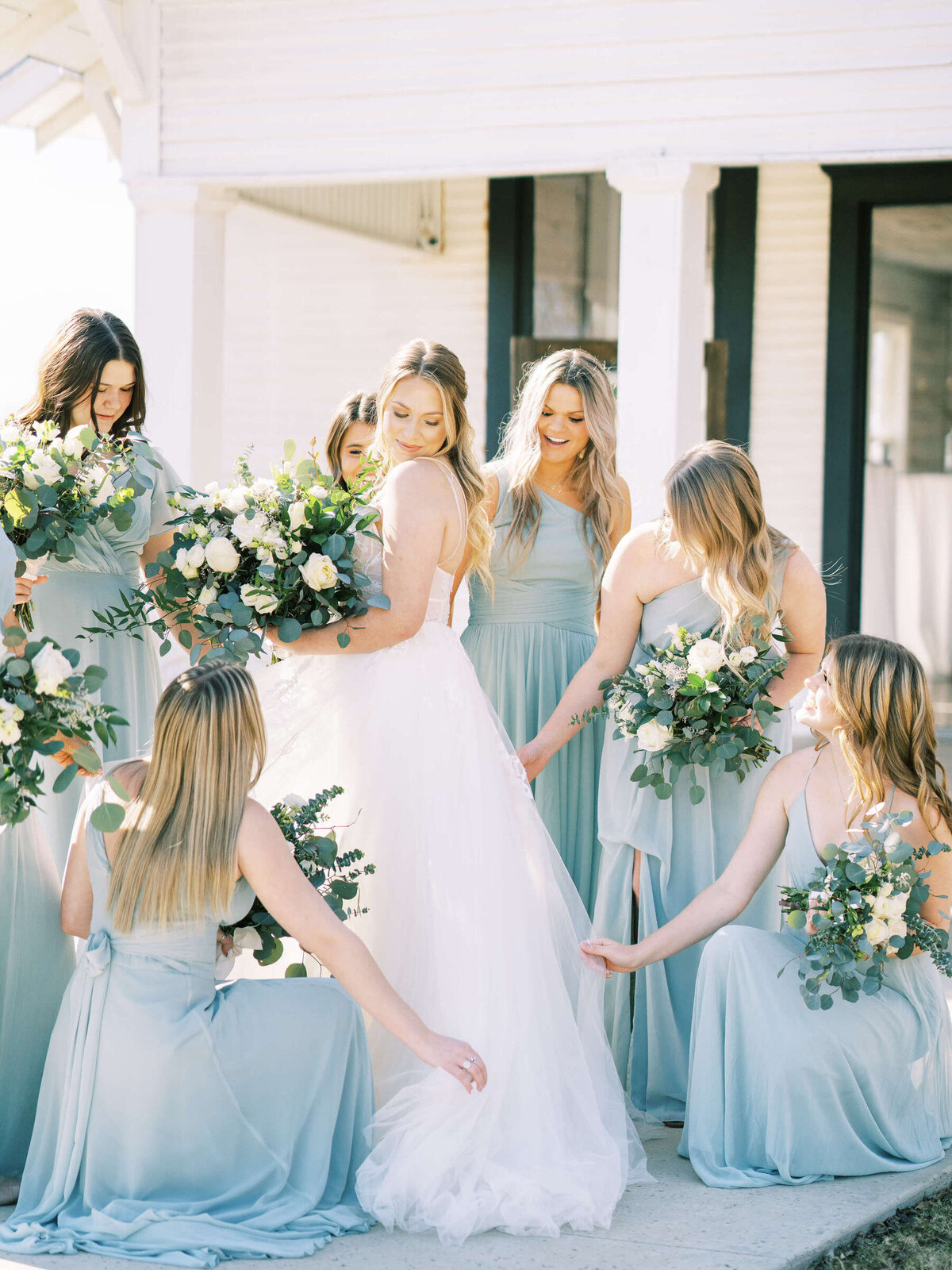 Bridesmaids in light green dresses fluff bride's tulle gown