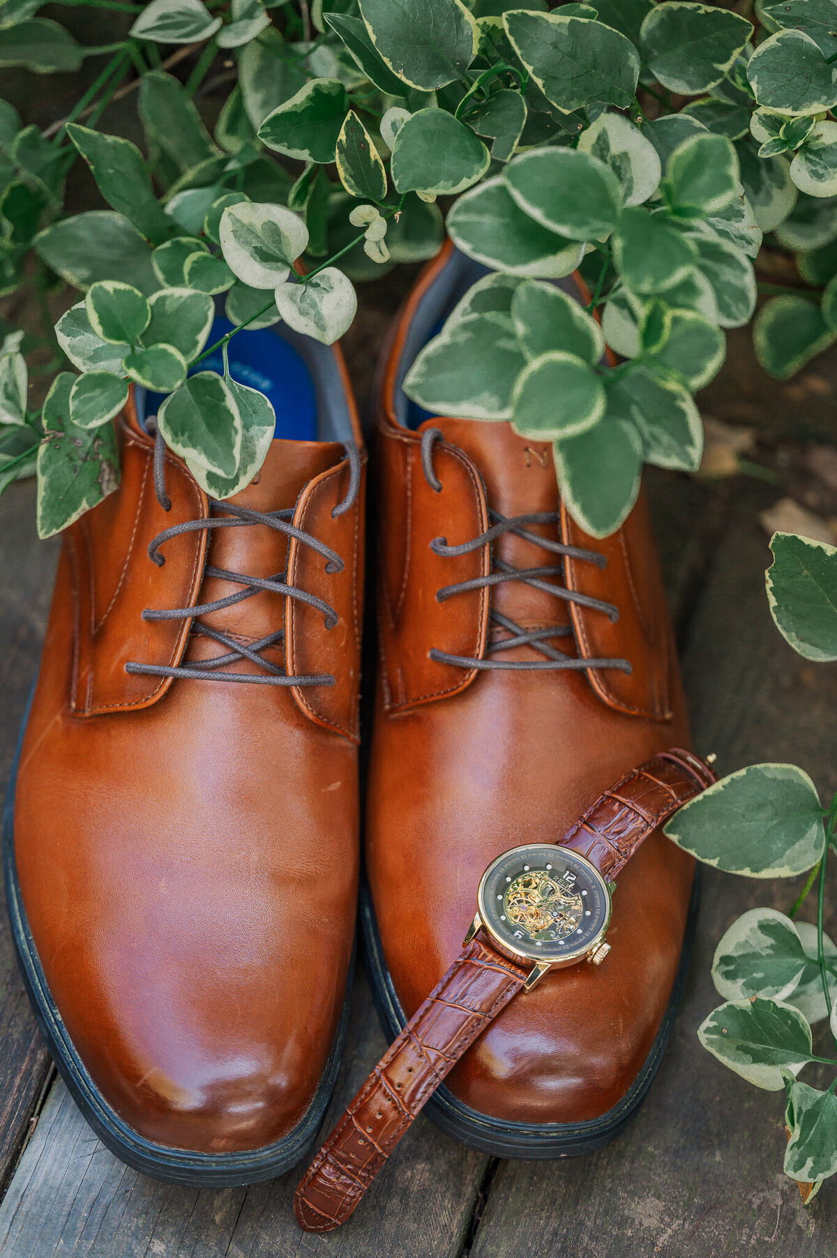 Brown shoes from a groom next to a bush by JoLynn Photography