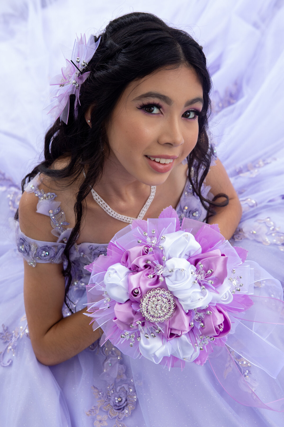 A teenage girl in a purple ballgown poses for a photo holding purple and white flowers New York Westchester quinceanera Photographer Milestone images