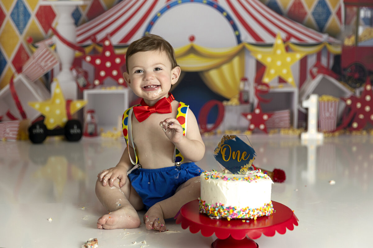 A young toddler sits in suspenders for a circus themed birthday photo shoot