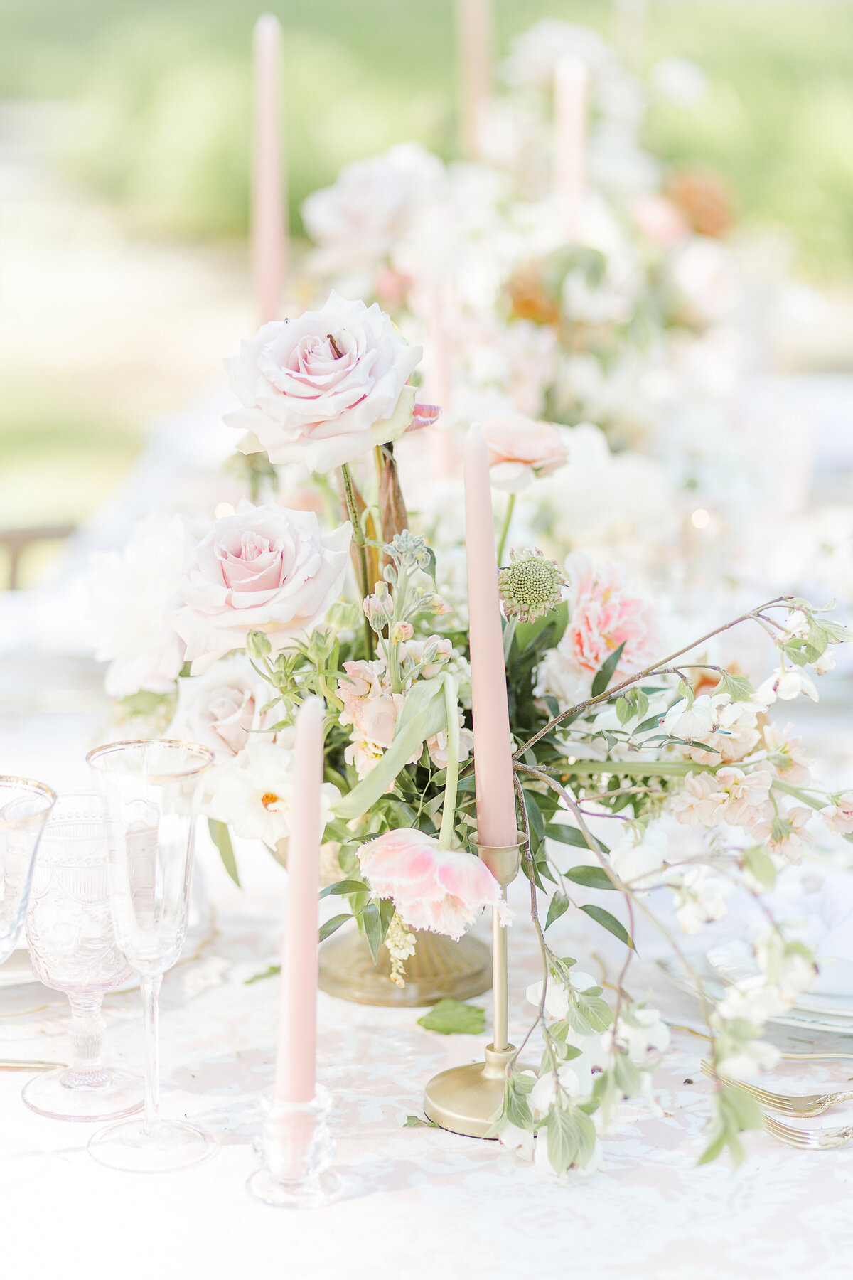 A tablescape is captured featuring pink blooms with greenery, and brushed gold candlesticks and flatware. Captured by Lia Rose Weddings