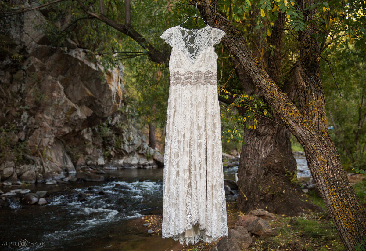Evergreen Colorado Wedding photographer lace bohemian wedding gown hangs creekside at Bear Creek Cabins