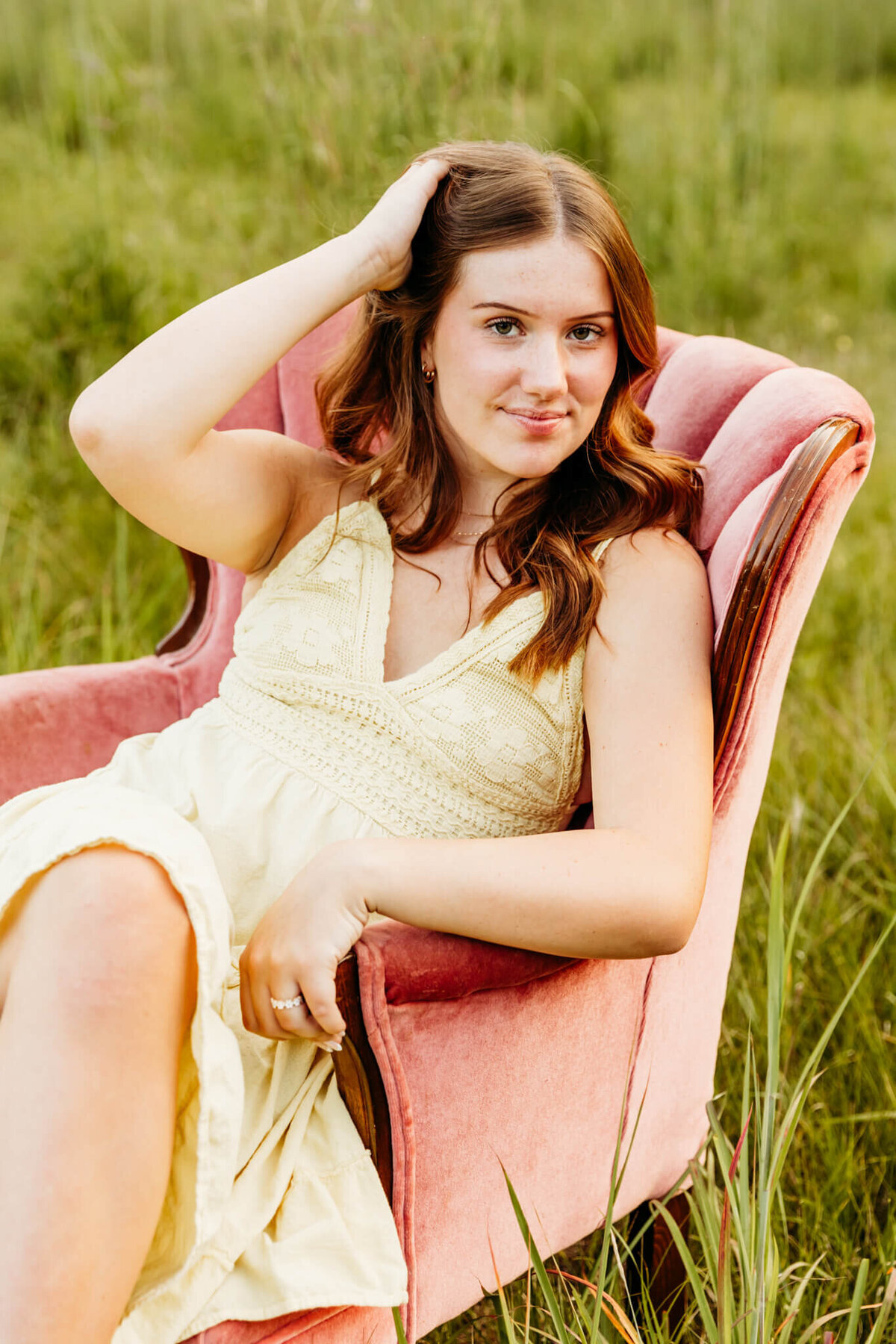 soon to be senior in high school sitting in a pink velvet chair and  pulling hair back captured by Green Bay Senior Photographer Ashley Kalbus