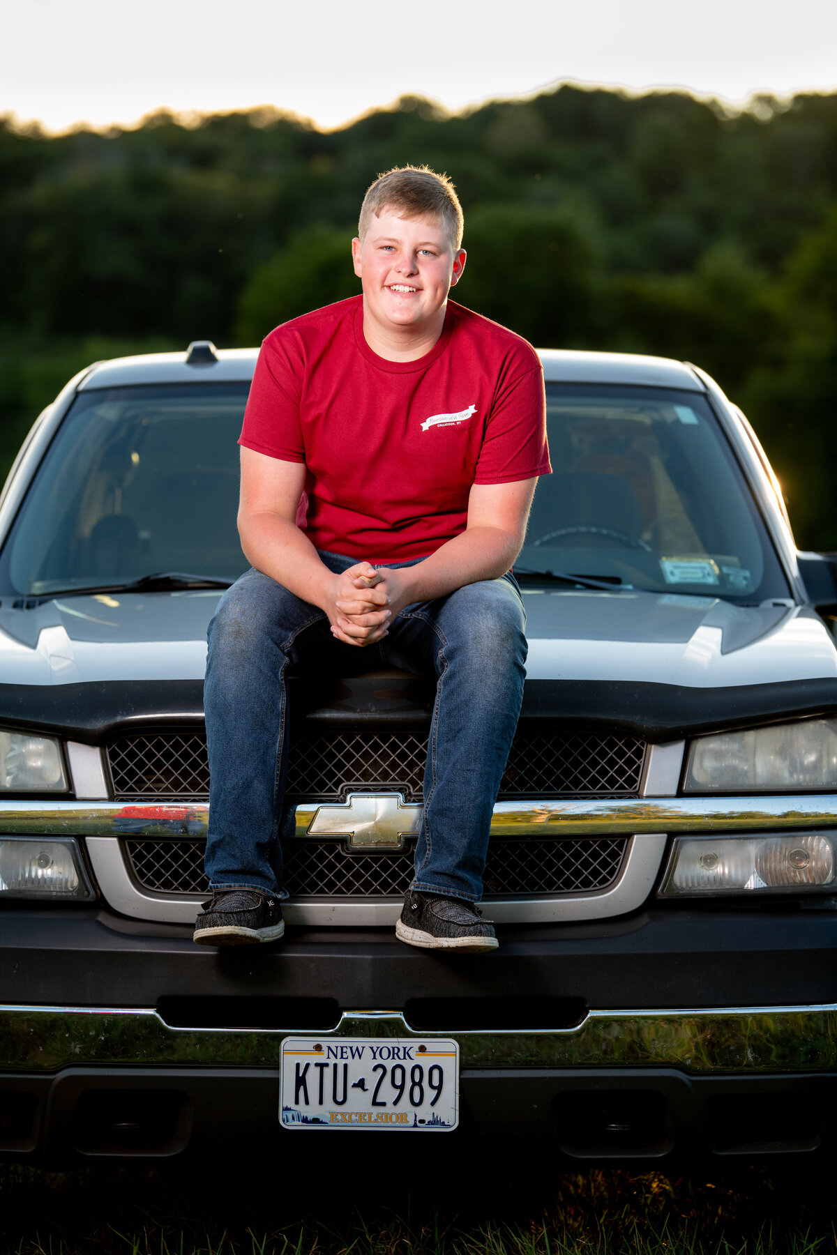 a teenage boy sits on the hood of his pick-up truck during his senior photo session