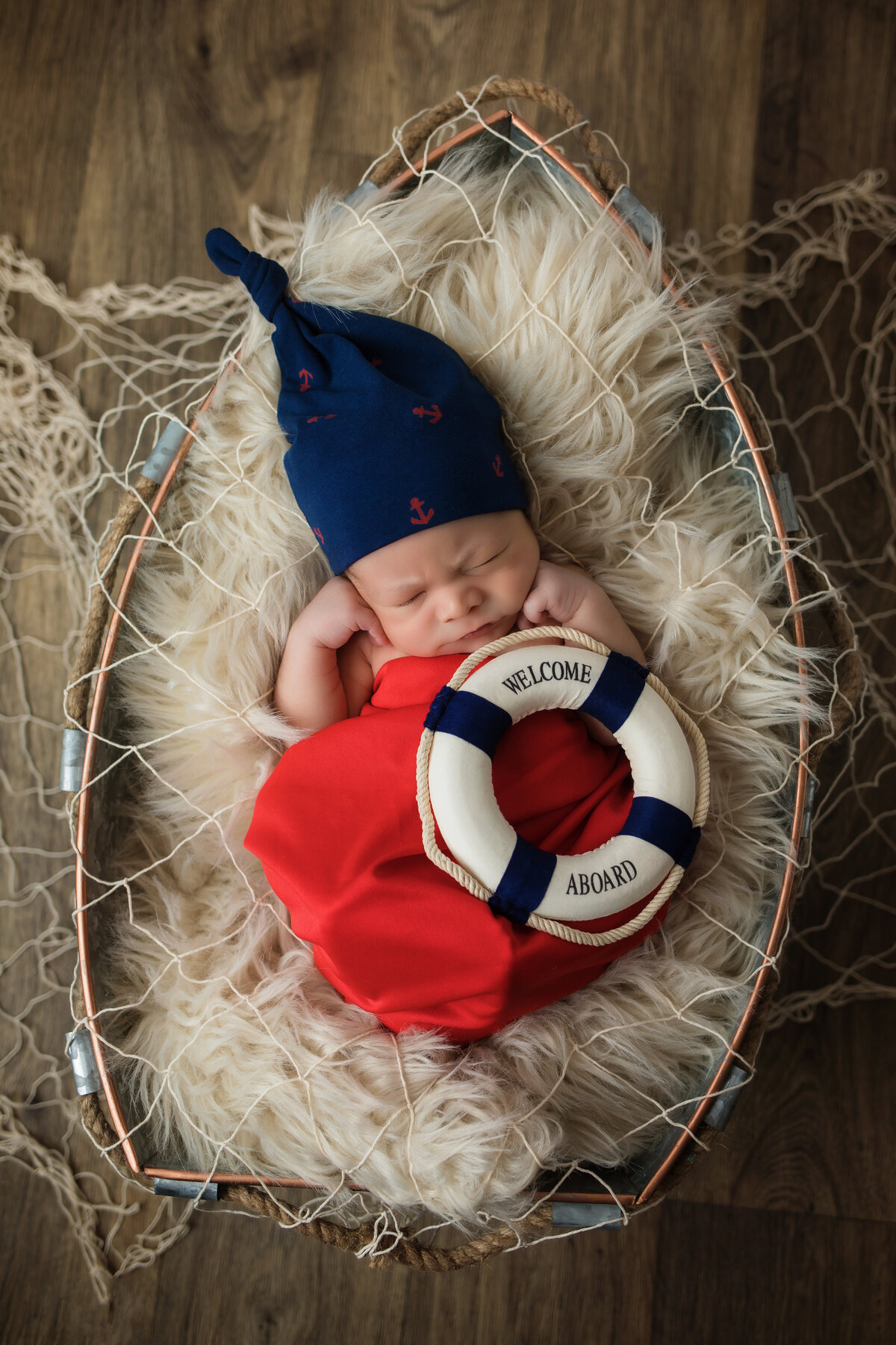 Newborn Photographer, a baby sleeps in a boat shaped basket with a knit cap and holds a lifesaver