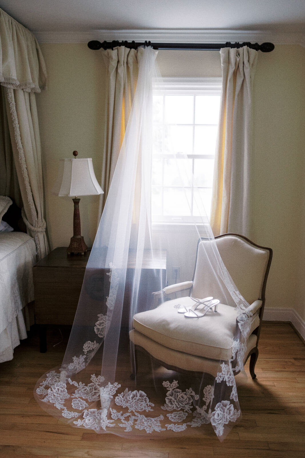 The bride's wedding footwear is on a couch, covered with her veil, which is hanging from the window, at The Lion Rock Farm, CT.