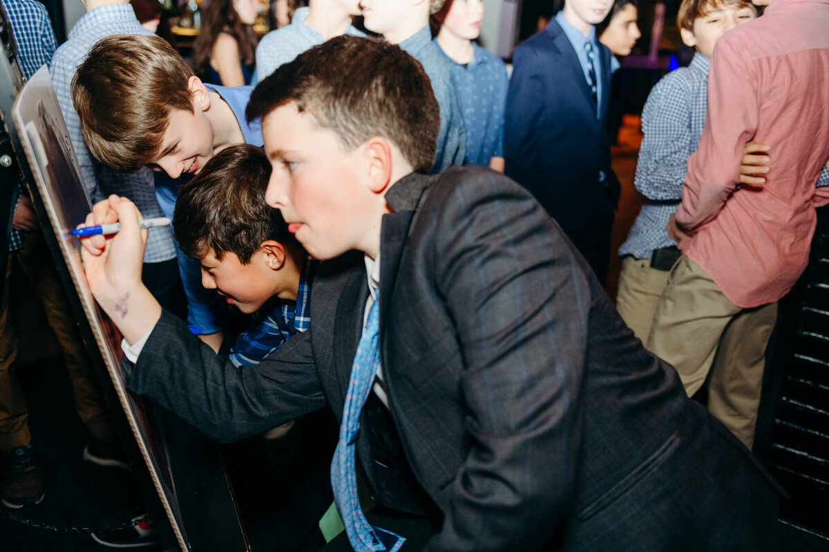 A boy signs a poster for a bar mitzvah while wearing a suit for some Bellevue Bar and Bat Mitzvah Photography