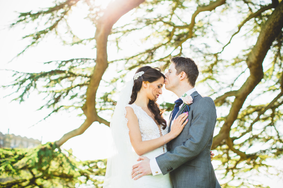 bride and groom kissing in the grounds at allerton castle under a tree with sun shining