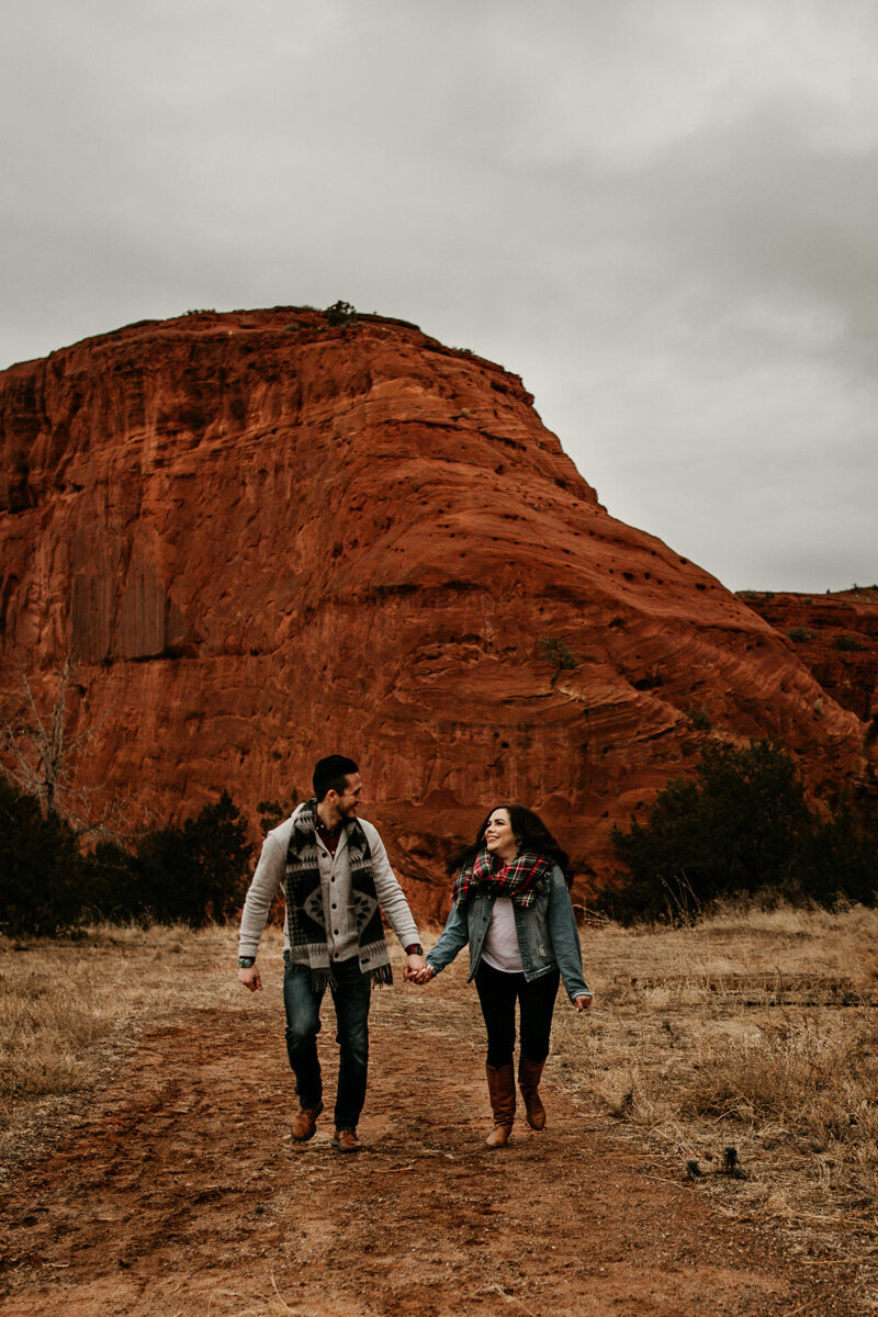 engaged couple walking in front of a red rock mountain