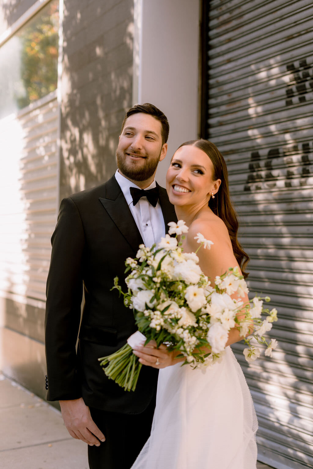 bride and groom standing next to each other smiling while she holds a bouquet