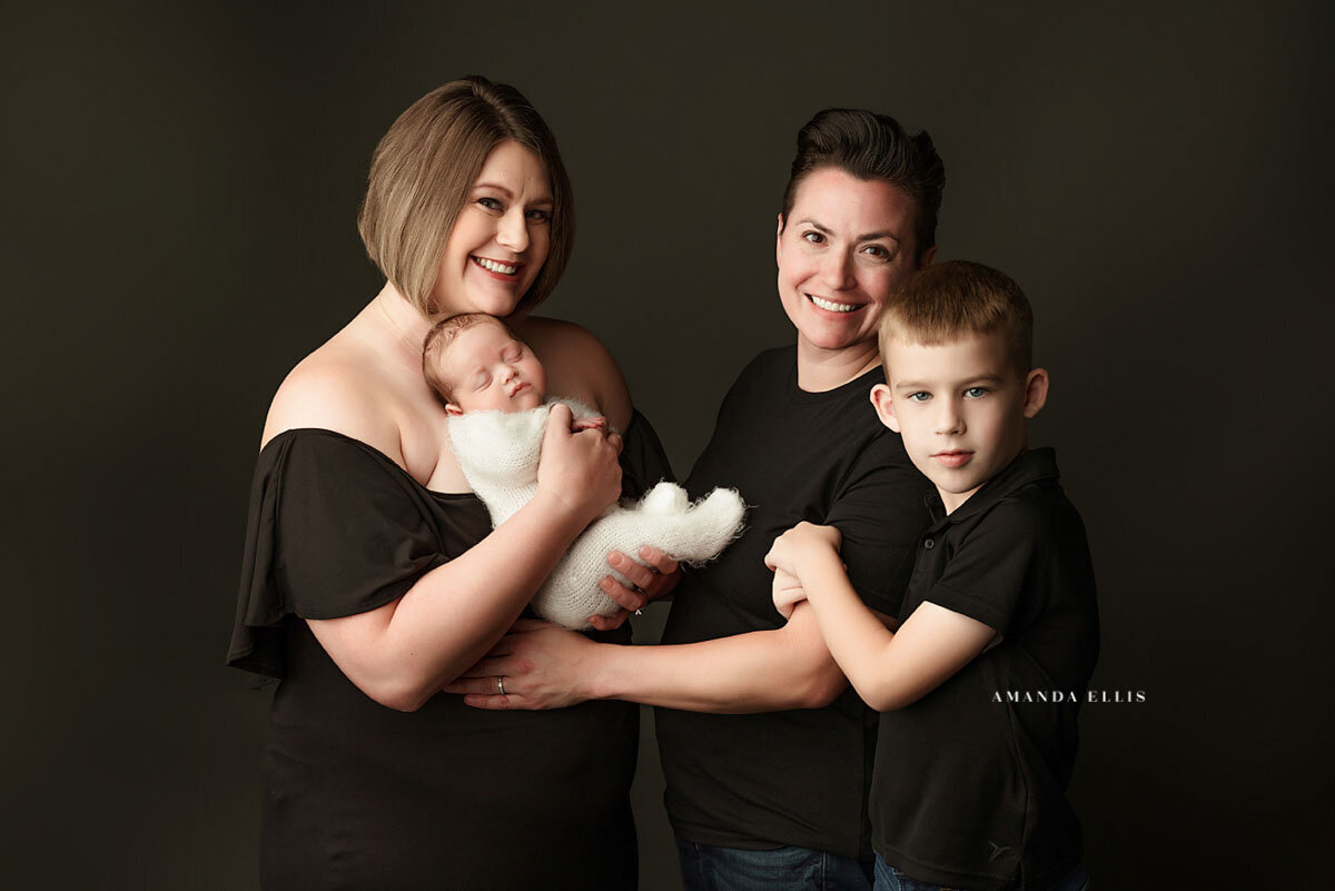 Dark and moody family portrait of two mothers with their son and newborn