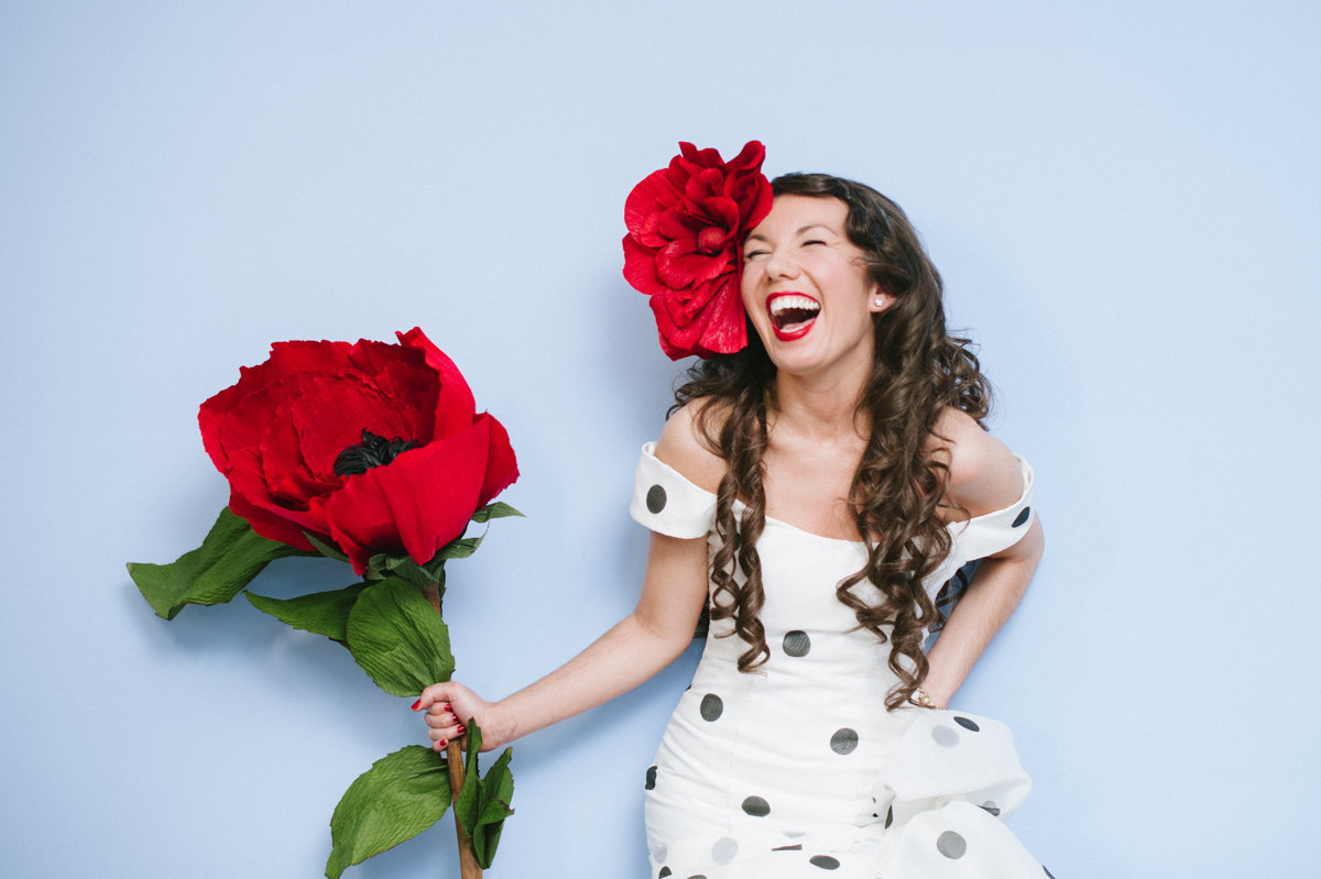 Alternative bride with single large red paper flower on a blue wall
