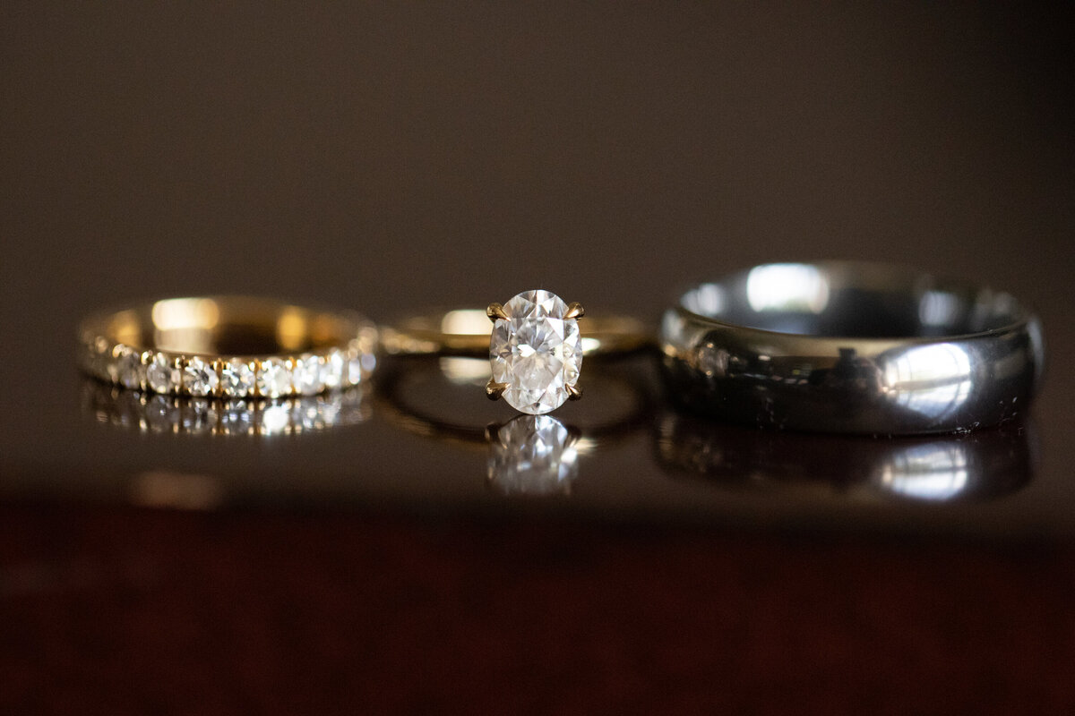 still lifee of women's wedding ring engagement ring and man's wedding band on a glossy brown surface Briarcliff Manor Wedding Photographer Milestone Images