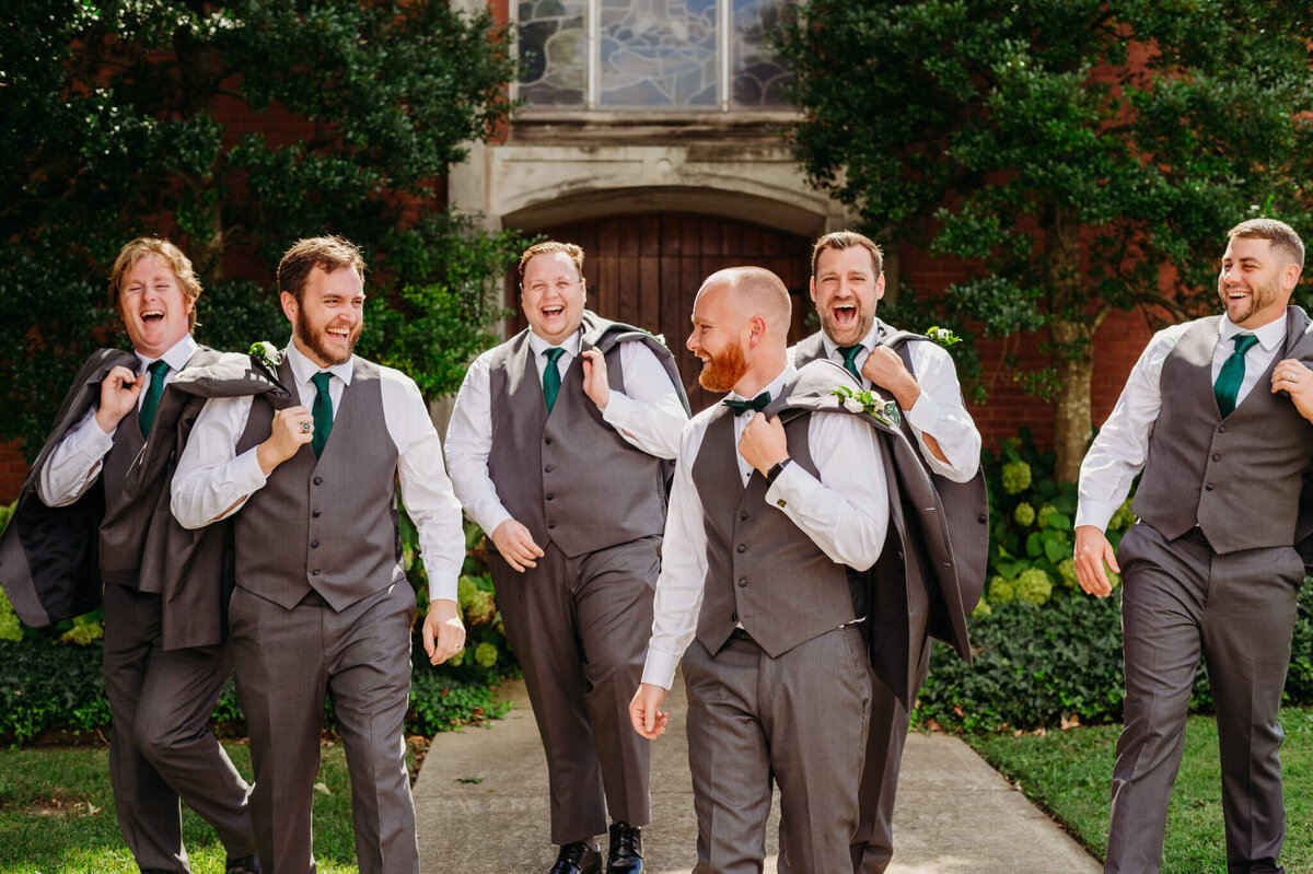 Photo of a groom and groomsmen with their jackets hanging over their shoulders as they walk and laugh
