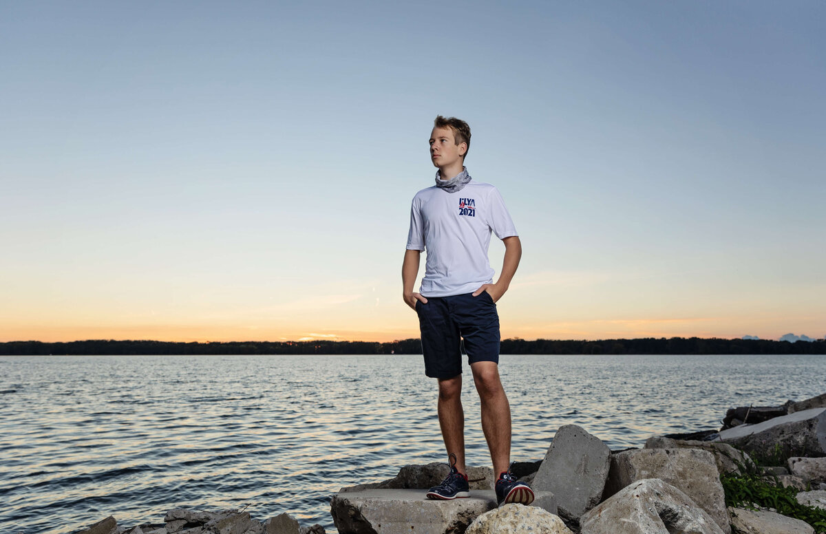 Senior photo of a boy standing on rocks looking off into the distance at sunset on the Erie Pa bayfront