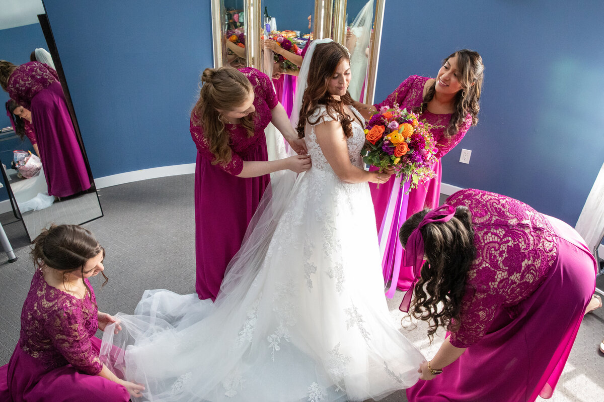 Six bridesmaids in fuschia dresses help a bride holding a bouquet wearing a white dress Mamaroneck Beach and Yacht Club Westchester New York wedding photographer Milestone Images