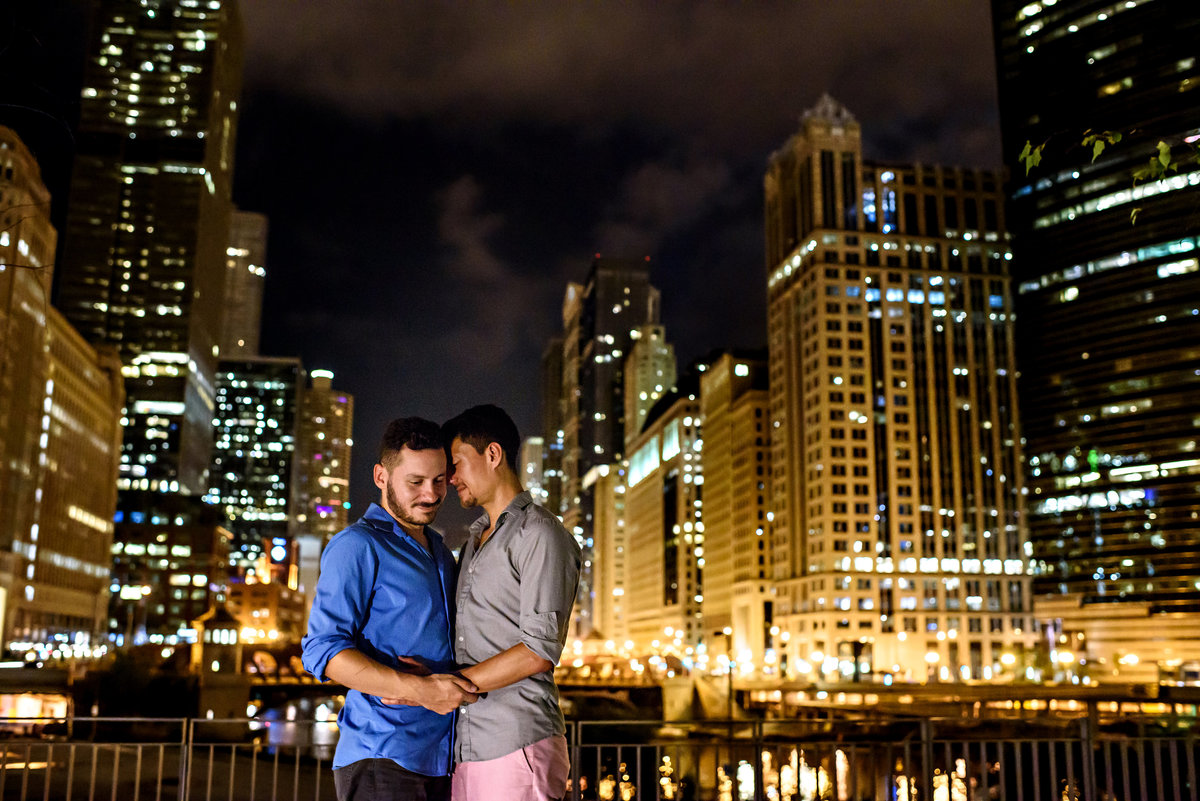 A gay couple in front of the Chicago cityscape at night.