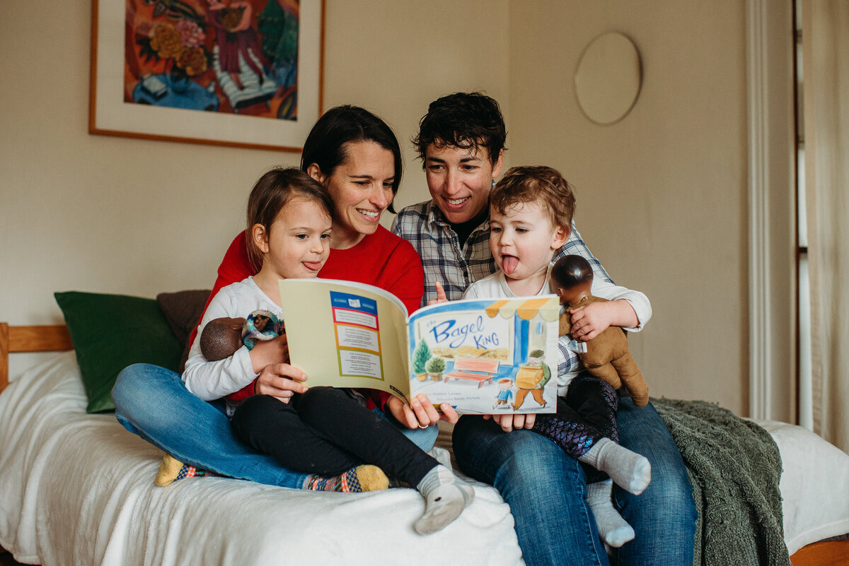 family with two moms read books to children on bed