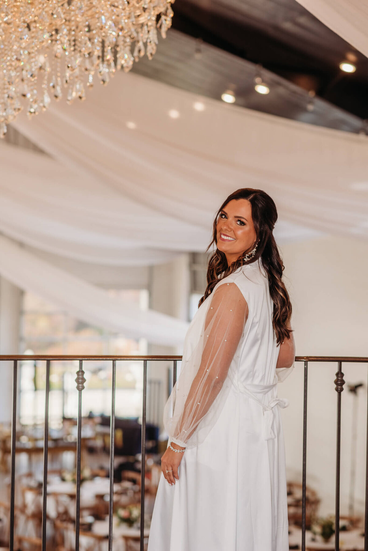 photo Of a bride in a white robe standing on a balcony with a chandelier in the background