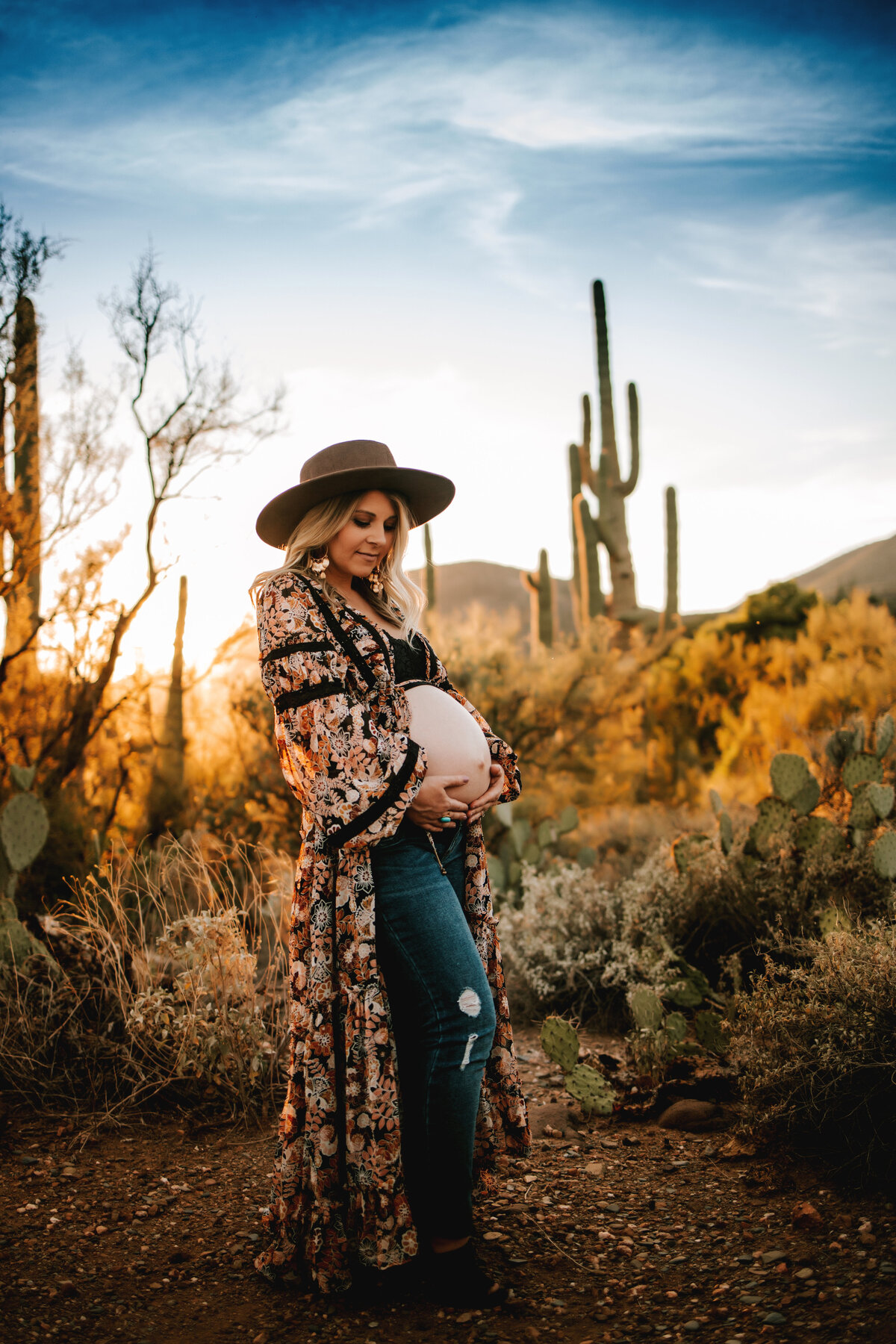 prenant mom holds bare belly whilte wearing a long duster and jeans in arizona for maternity session