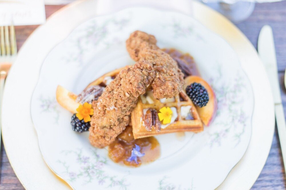 Elegant plated brunch featuring fried chicken and waffles with fresh blackberries, peaches, pecans, and edible flowers, served on vintage china at The Seclusion wedding venue in Virginia.