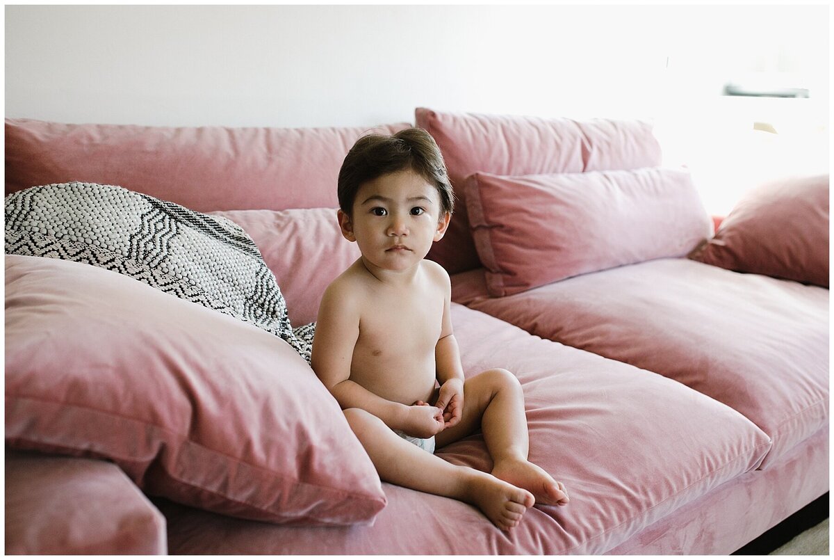 child wearing a diaper sitting on pink velvet sofa at  family session at home in Austin Texas