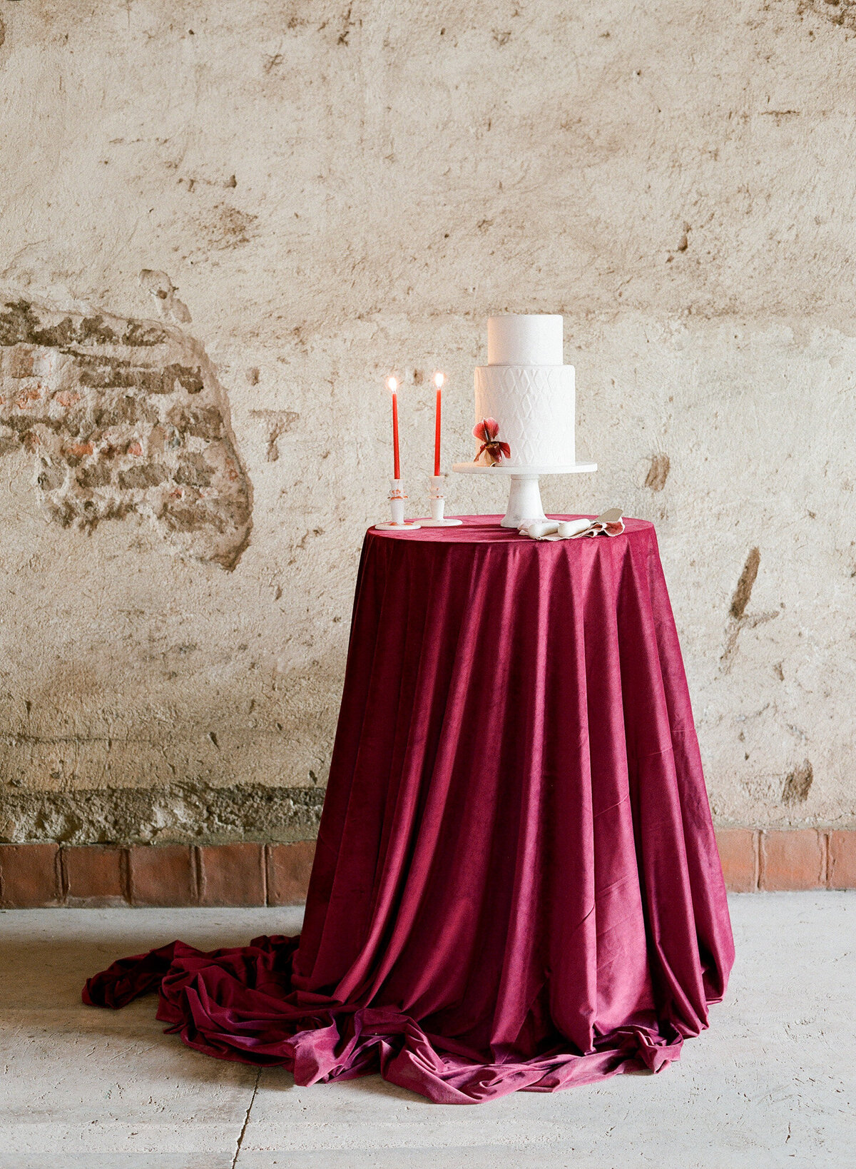 White cake and red candles placed on a tabletop with red velvet tablecloth.