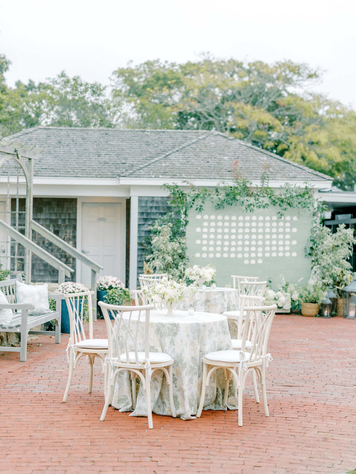 Outdoor wedding reception with floral tablecloths and a green seating chart display decorated with greenery