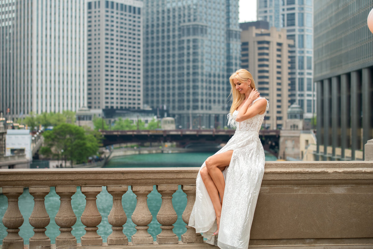 Bride showing her long legs  while sitting on the edge of the railing by  Chicago river on of the most popular photoshoot locations