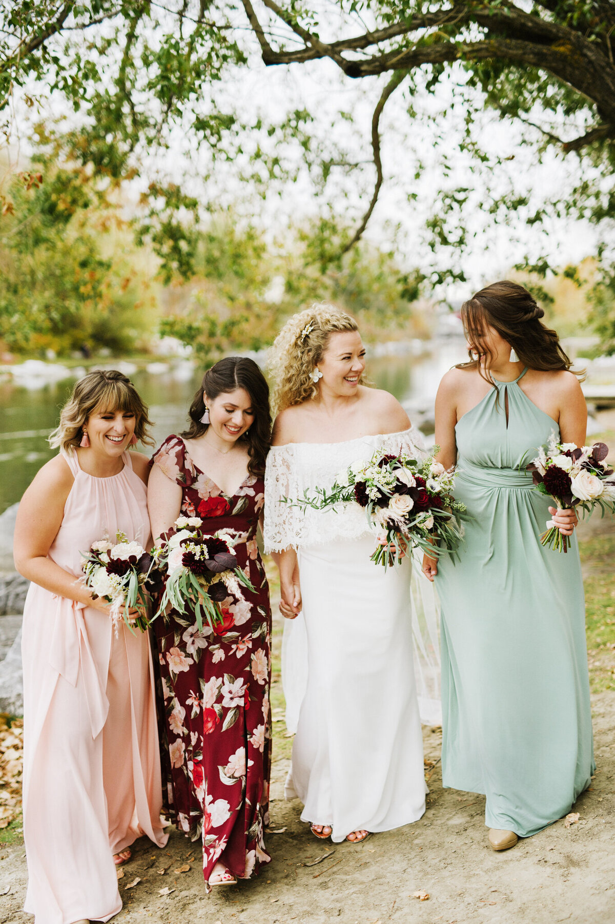 Bride in an off-the-shoulder boho inspired lace gown, with bridemaids in mismatching dresses holding Burgundy and pink autumn florals, captured by Christy D. Swanberg Photography, editorial elopement and wedding photographer in Calgary, Alberta, featured on the Bronte Bride Vendor Guide.