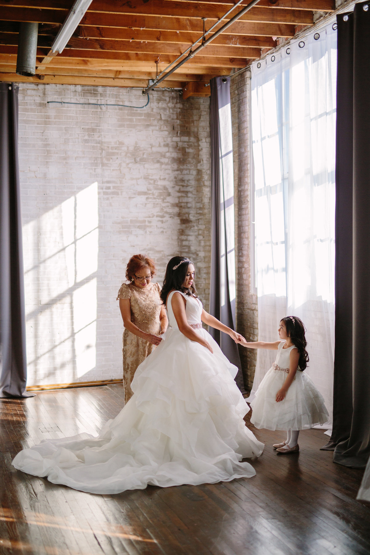 Bride holding flower girls hand while mother of bride buttons gown in downtown San Antonio wedding