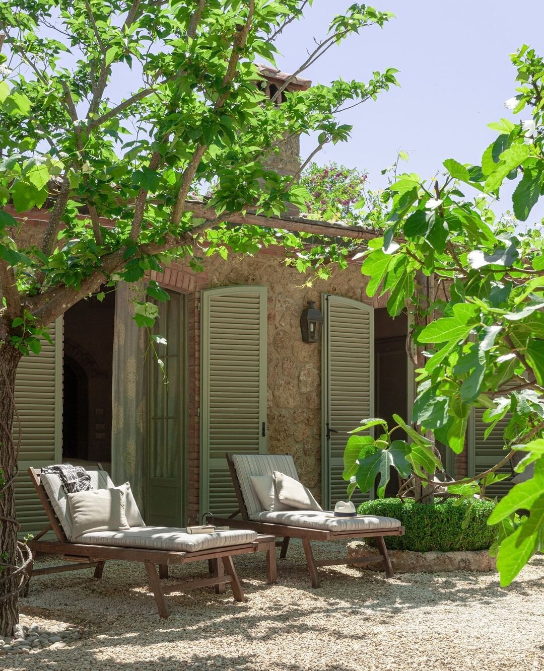 Lounge chairs in front of an Italian stone building with sage green shutters at Borgo Santo Pietro