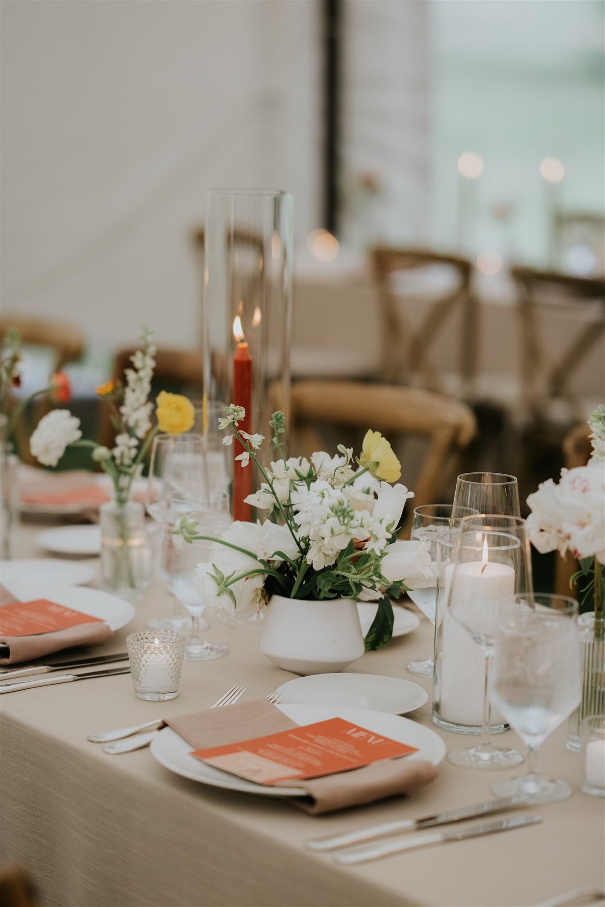 Long Table at a wedding reception with taupe linens wood chairs white candles and orange menu cards at Ankony Carriage House in the Hudson Valley with Hudson Valley Wedding Planner Canvas Weddings