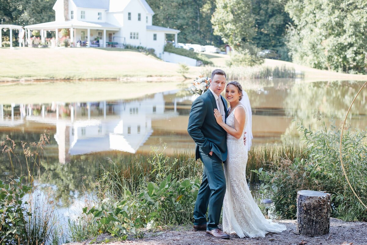 bride and groom smiling while standing in front of a pond