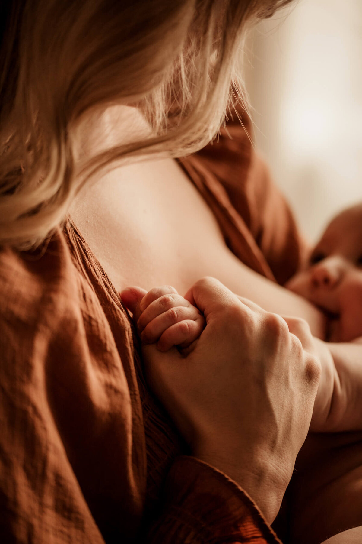 Woman holds her son's hand in hers as she nurses him and he smiles at her.