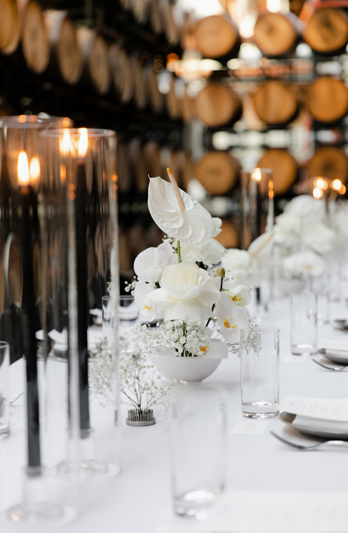 White lilies and baby's breath paired with black candlesticks decorate wedding reception tables at Moody Tongue Brewery.