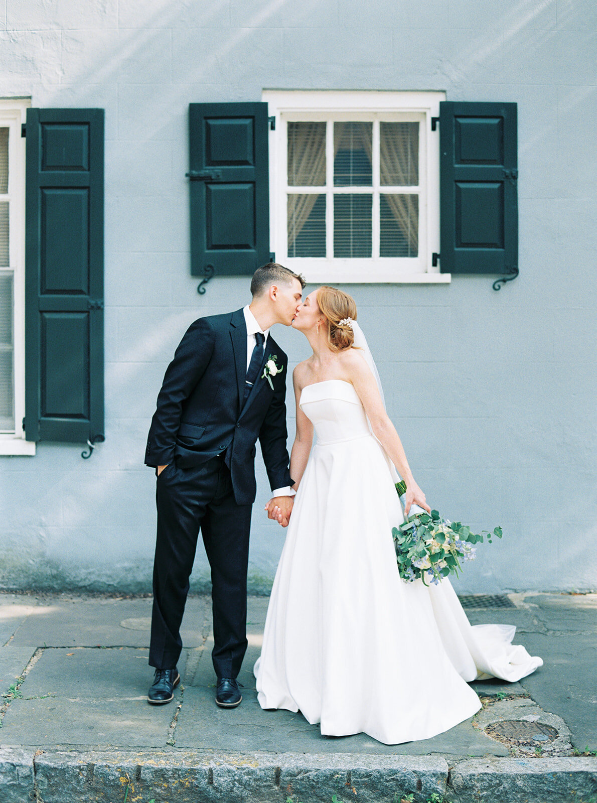 Charleston film wedding photo of bride and groom leaning in for a kiss. Background is light blue Charleston wall.