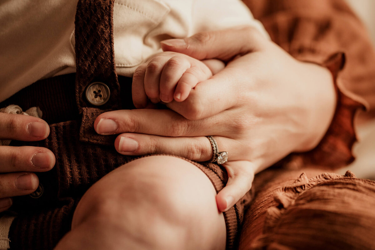 Mother holds her baby boys tiny hand.