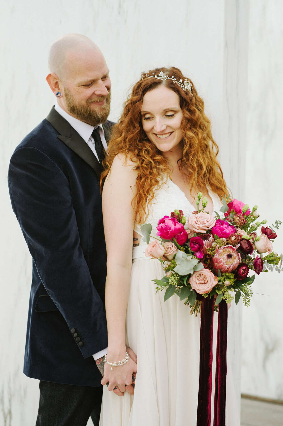 Bride and groom holding hands, gorgeous orange hair with stunning bridal hairpiece, holding bright pink and fuchia bouquet, captured by Christy D. Swanberg Photography, editorial elopement and wedding photographer in Calgary, Alberta, featured on the Bronte Bride Vendor Guide.
