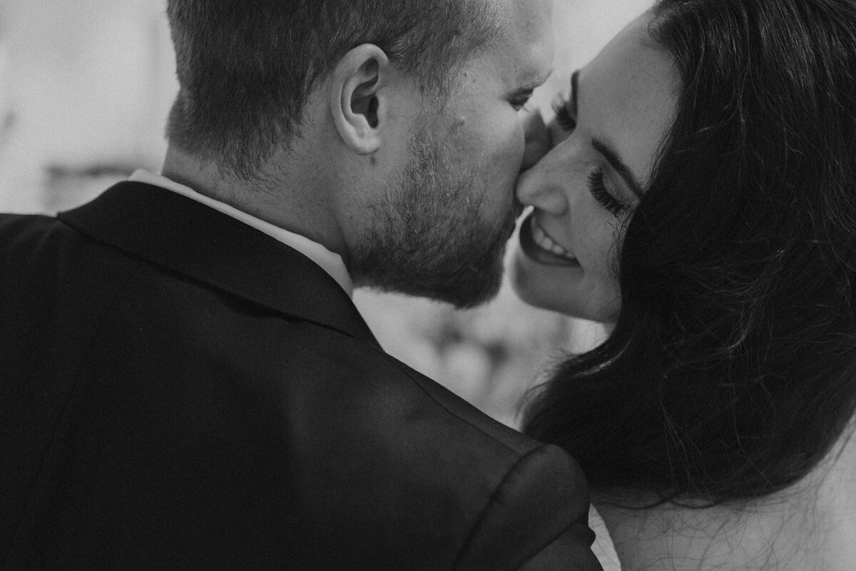 the-groom-is-kissing-bride-and-she-is-smiling-black-and-white-photo