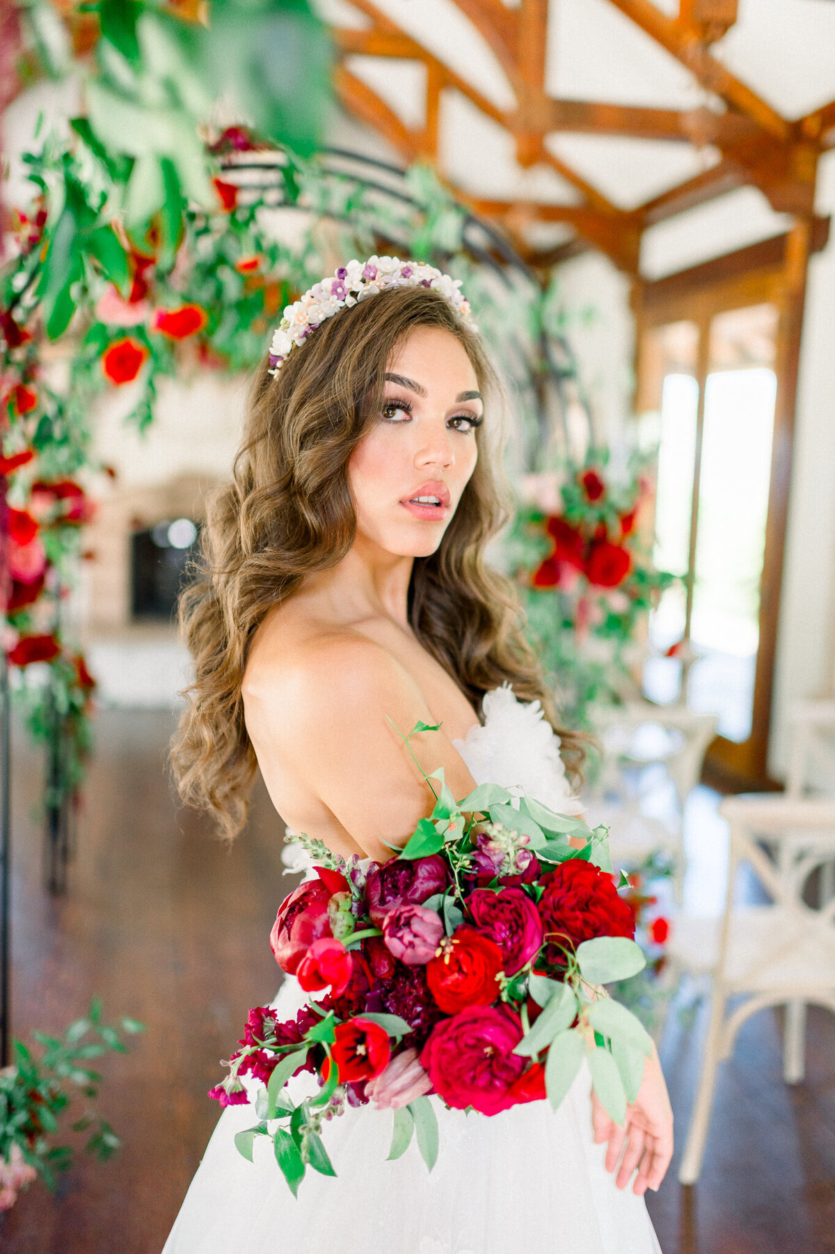 bride with floral crown and red flowers poses for camera by arkansas wedding photographer