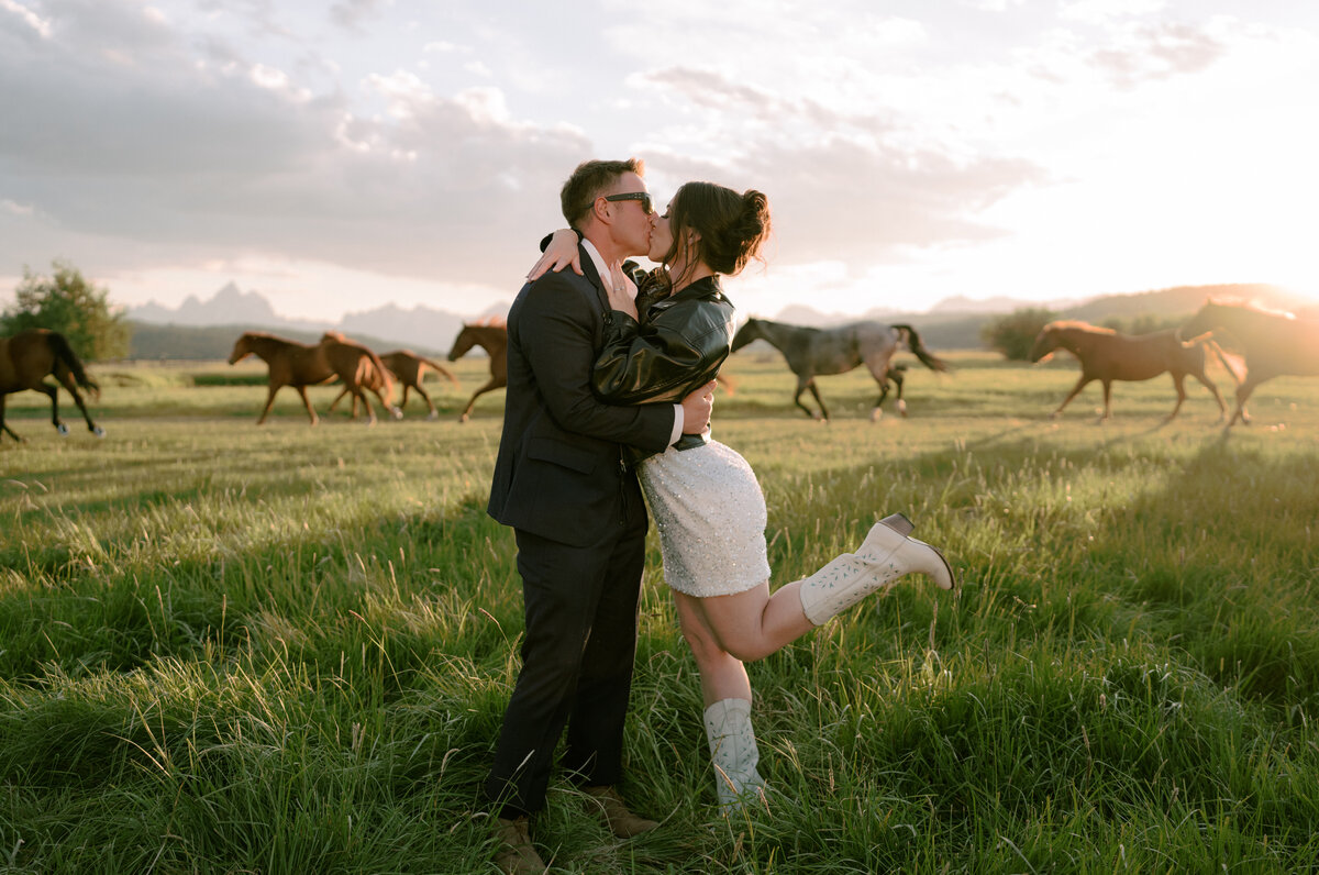 Bride and groom kissing with horses running in the background for a summer wedding in Jackson, WY.