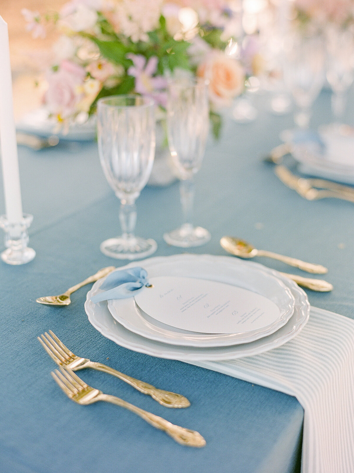 table plates with golden silverware on a table with a blue tablecloth and pastel florals in the background