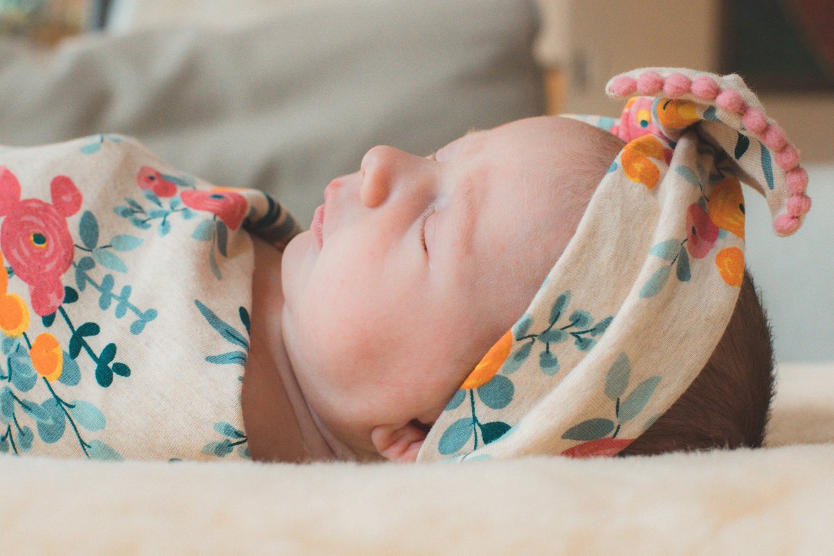 newborn baby in floral swaddle and headband
