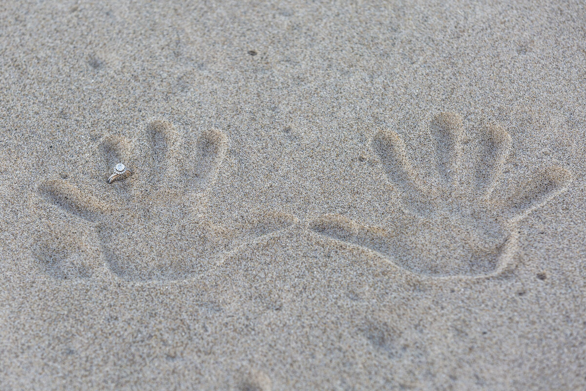 Sand handprint with a ring photo on a beach.