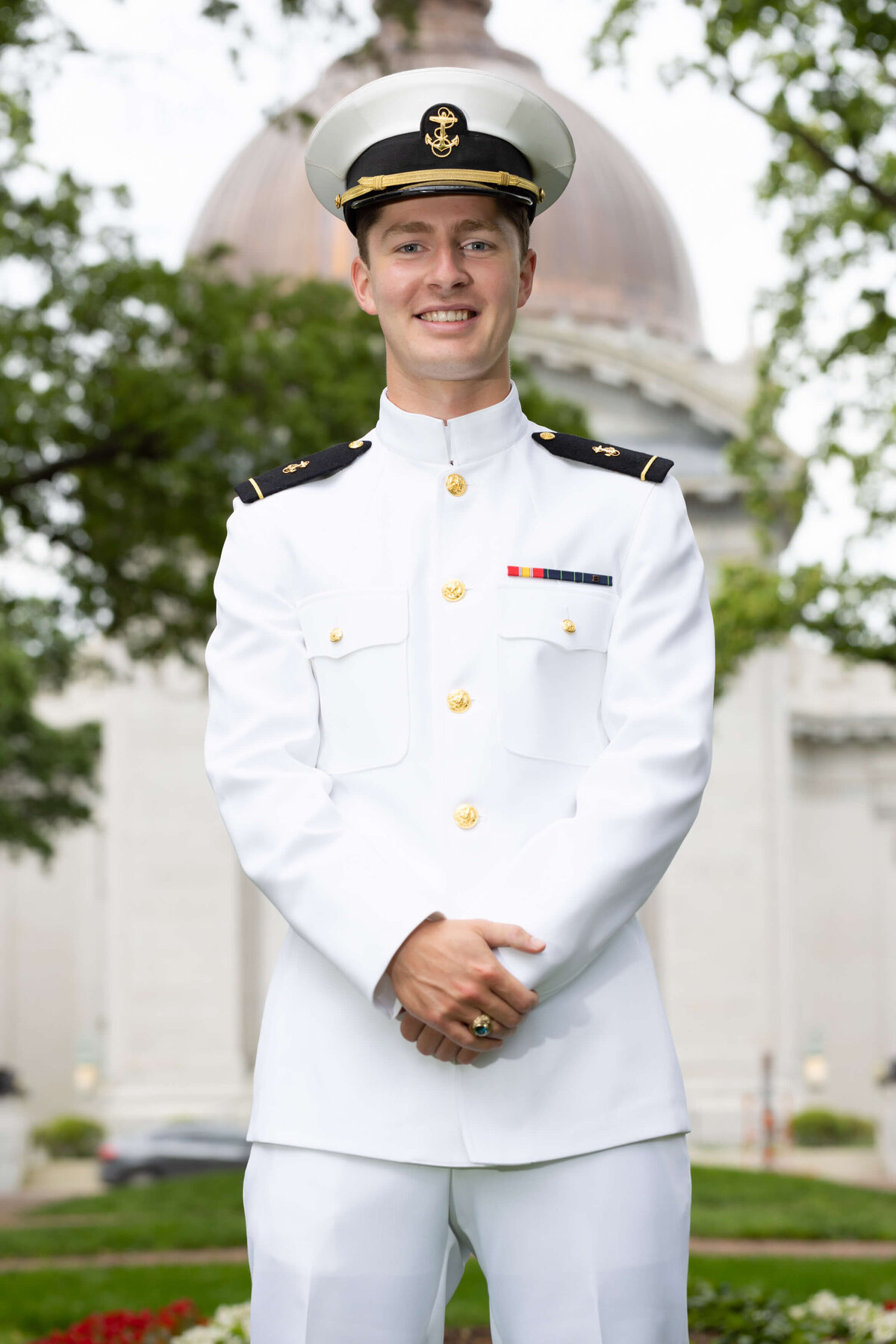 Senior portrait in white navy uniform in front of the Naval Academy Chapel dome.
